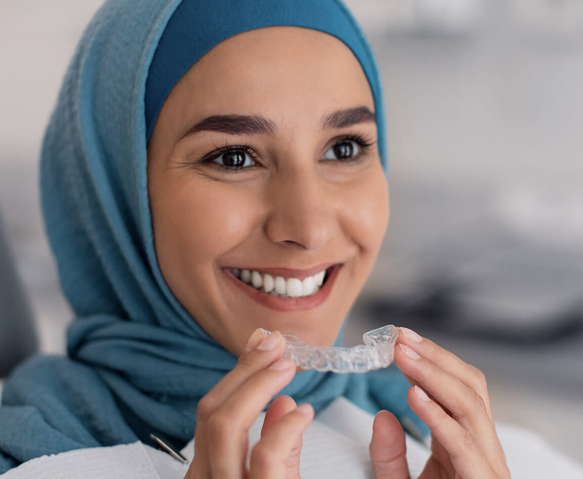 A patient holding her clear aligner and smiling